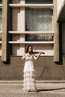 A woman artist with dark hair in a dress holds a wooden concert electric violin in her hands photo