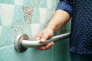 Asian woman patient use toilet support rail in bathroom, handrail safety grab bar, security in nursing hospital. photo