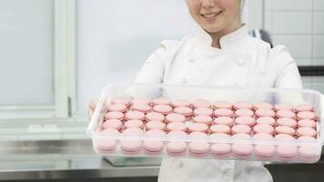 tondu coup de une Pâtisserie chef souriant en portant en dehors plateau avec rose macarons video