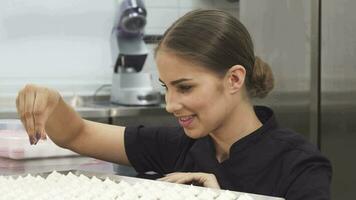 Beautiful female pastry chef decorating meringues with coconut flakes video