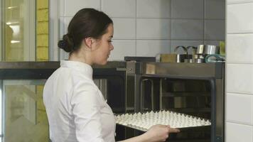 Young beautiful female confectioner putting merengues into the oven video