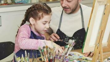 Cropped shot of a cute little girl smiling talking to her dad mixing paints at art class video