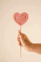 a person holding a pink heart shaped lollipop photo