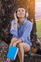 Woman  relax time in park. she listening music under big tree. photo