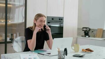 Freelancer woman talking on the phone and laughing while working at home. video