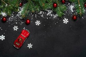 Christmas or New Year decoration background model miniature red car. For fir tree branches on black background with copy space. Flat lay. Pattern. White snowflakes and snow, red balls photo