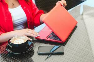 un niña en trabajos en un ordenador portátil en un café con un capuchino y un teléfono. foto