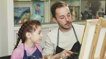 söt liten flicka tittar på henne far konstnär målning en bild video