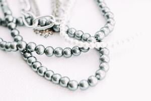 A necklace of gray beads with chain decorations on a white aesthetic background. photo