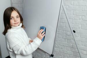 Little girl standing and cleaning whiteboard. Child smiling and looking at camera photo