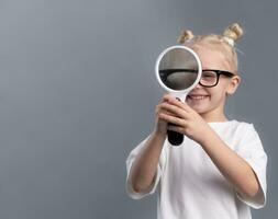 curious child smiling and looking through magnifying glass on gray background. Portrait of curious little girl holding magnifier, copy space photo