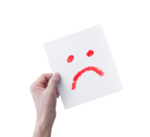 Hand holding white paper with hand drawn unhappy face emoticons isolated on transparent background. PNG Format