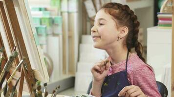 fofa pequeno menina mostrando polegares acima enquanto pintura uma cenário às a arte classe video