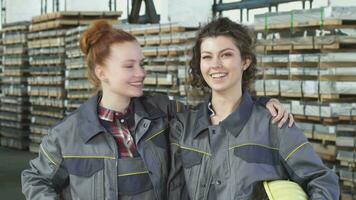 zwei glücklich weiblich Fabrik Arbeitskräfte Umarmen zeigen Daumen oben beim das Lager video