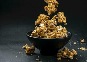 Peanut kozinaki falling in bowl on black background photo