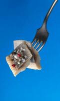 Pieces of salted herring on fork isolated on blue background photo