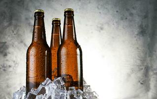 frío ligero cerveza con agua gotas, cerveza botellas con hielo cubitos foto