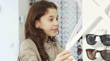 Cute little girl choosing sunglasses from the display at the shopping mall video