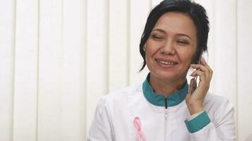 Beautiful Asian mature female doctor talking on the phone smiling joyfully video