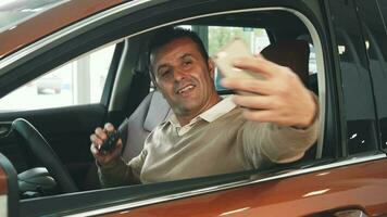 A cheerful man sitting in the car makes selfie with keys video