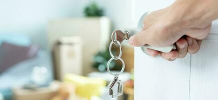 Moving house, relocation. The key was inserted into the door of the new house, inside the room was a cardboard box containing personal belongings and furniture. move in the apartment, banner photo