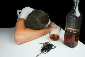 coche llaves y alcohol en el mesa. borracho hombre dormido en el mesa con botella de whisky y beber. alcoholismo. no lo hagas conducir cuando estás borracho. foto