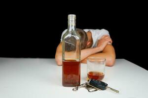 Car keys and alcohol on the table. Drunk man sleeping on the table with bottle of whiskey and drink. Alcoholism. Don't drive when you're drunk. photo