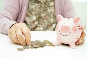 Retired elderly woman counting coins money with piggy bank and worry about monthly expenses and treatment fee payment. photo