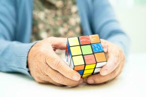 bangkok, Tailandia agosto 14, 2023 Alzheimer enfermedad anuncio, asiático mayor mujer paciente jugando rubik cubo juego a práctica cerebro formación para demencia prevención. foto