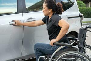 asiático invalidez mujer en silla de ruedas consiguiendo en su auto, accesibilidad concepto. foto