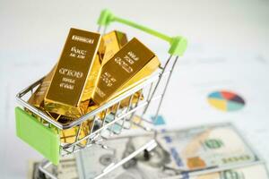 Gold bar in shopping cart on US dollar banknotes money and graph, economy finance exchange trade investment concept. photo