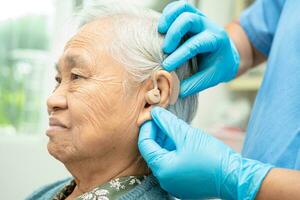 audiólogo o ent médico utilizar otoscopio comprobación oído de asiático mayor mujer paciente tratando escuchando pérdida problema. foto