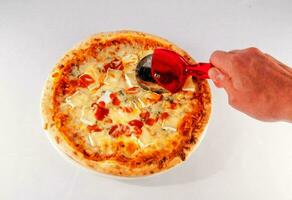 a person is holding a pizza cutter over a pizza photo