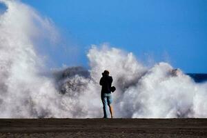 a person is standing on the beach looking at a large wave photo