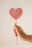 a person holding a pink heart shaped lollipop photo