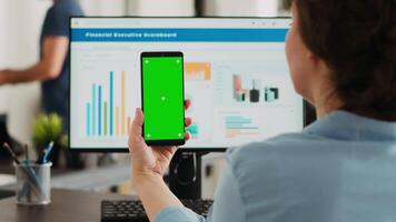 Businesswoman showing greenscreen display in coworking space, holding device with isolated copyspace layout on screen. Person using smartphone with mockup chromakey template. video