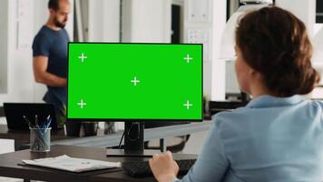 Worker using greenscreen display on pc monitor, looking at isolated mockup template in coworking space. Creative agency employee checking blank chromakey screen on computer, startup company. video