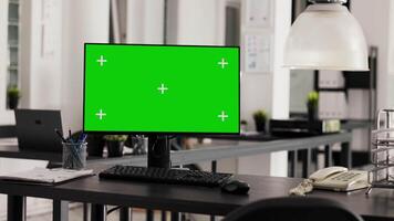 Empty office desk with pc running greenscreen on display, showing isolated chromakey template in coworking space. Workstation in open floor plan with monitor and copyspace layout. video