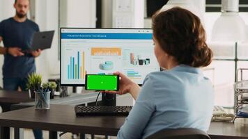 Office worker looks at greenscreen on smartphone display app, analyzing isolated chromakey layout on mobile device at work. Woman holding phone that shows blank mockup template. video