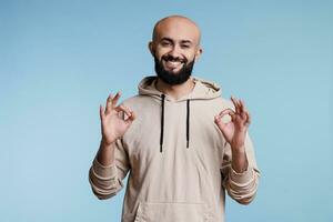 Smiling arab man showing ok gesture with two hands and looking at camera. Cheerful arabian bearded person posing with okay and agreement sign with fingers studio portrait photo