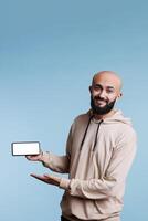 sonriente alegre árabe hombre demostración teléfono inteligente con blanco blanco pantalla para márketing burlarse de arriba retrato. despreocupado anunciante participación móvil teléfono con vacío monitor para aplicación promoción y mirando a cámara foto