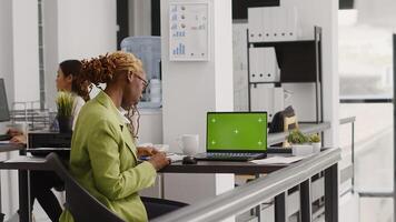 Young manager analyzing greenscreen template on laptop, using pc with chroma key display in office. Business entrepreneur looking at isolated blank mockup in agency coworking space. photo