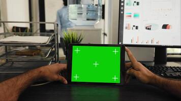 POV of manager uses tablet with greenscreen template, looking at chromakey layout and sitting in coworking space. Young man examining blank mockup copyspace on device display. video