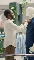 Vertical video Meticulous retail assistant working in luxury fashion boutique, arranging pocket square on blazer. Experienced african american employee showcasing new collection of trendy garments on