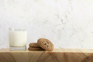 Glass of milk and cookies on wooden serving board, white textured wall as background. Copy space. photo