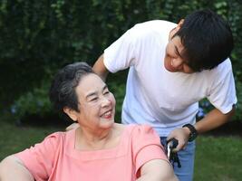 Portrait of Asian senior woman sitting on wheelchair with her son in the garden. photo