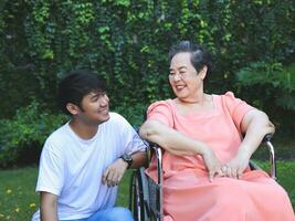 Portrait of Asian senior woman sitting on wheelchair with her son in the garden. photo