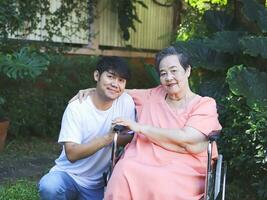 Portrait of Asian senior woman sitting on wheelchair with her son in the garden. photo