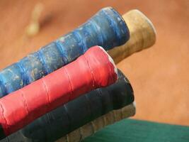 multi-colored tennis racket handles, worn from long training, close-up, blurred background, tennis court photo