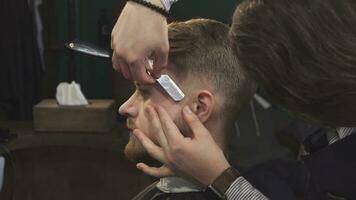 cerca arriba de un hermoso hombre consiguiendo afeitado con un maquinilla de afeitar por un Barbero video